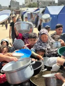 Displaced families in Gaza holding pots and bowls in line to receive food from Rammun Foundation