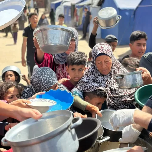 Displaced families in Gaza holding pots and bowls in line to receive food from Rammun Foundation