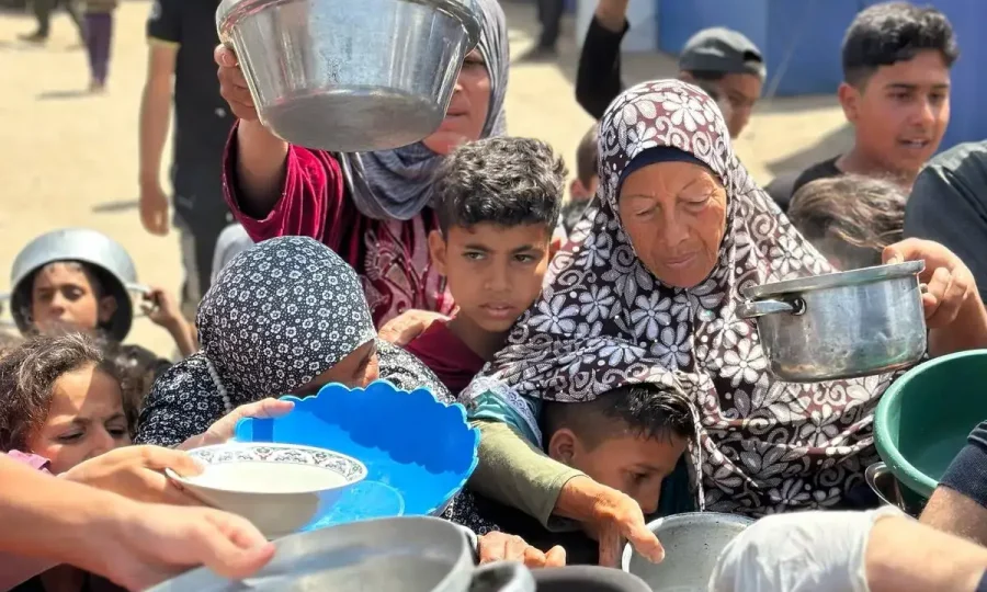 Displaced families in Gaza holding pots and bowls in line to receive food from Rammun Foundation