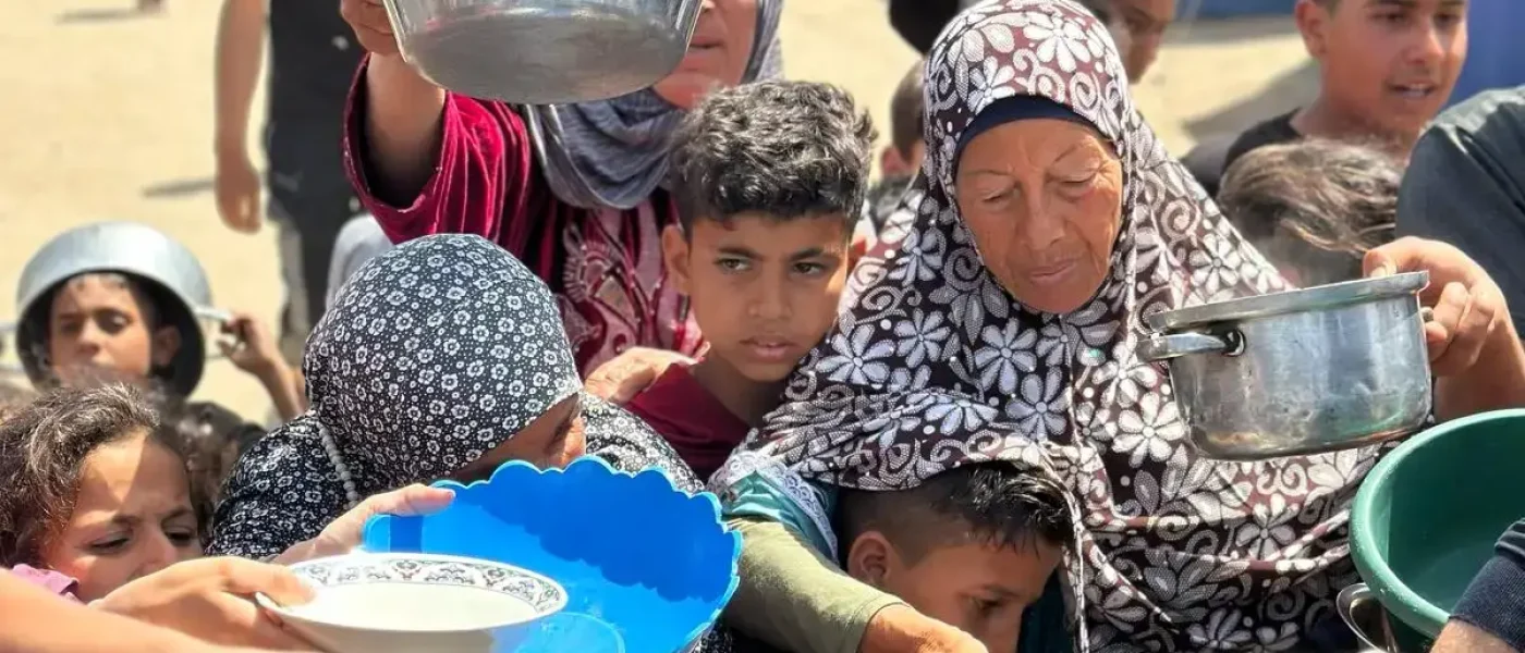 Displaced families in Gaza holding pots and bowls in line to receive food from Rammun Foundation
